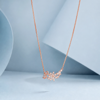 Rose gold floral necklace with zircon stones and pearl accents displayed on a pastel blue background.