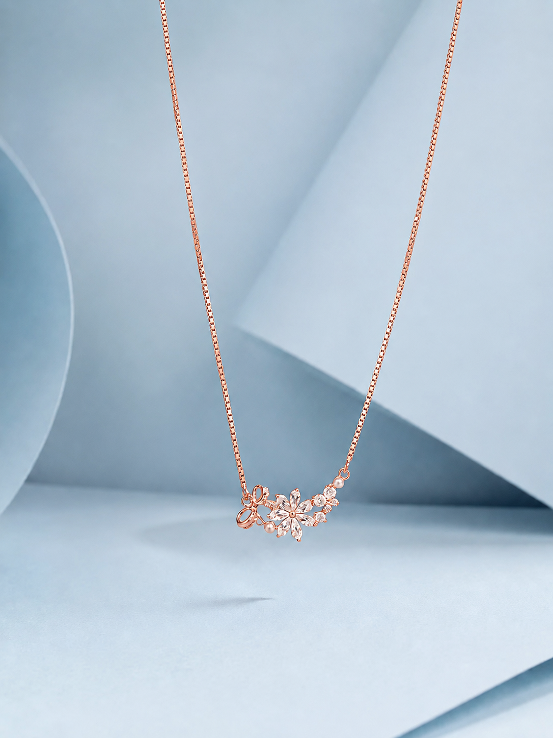 ChatGPT Image May 9, 2026, 03_50_03 PM Rose gold floral necklace with zircon stones and pearl accents displayed on a pastel blue background.