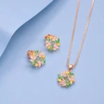 Rose gold floral pendant and earrings set featuring multicolour zircon stones displayed on a soft pastel blue background.