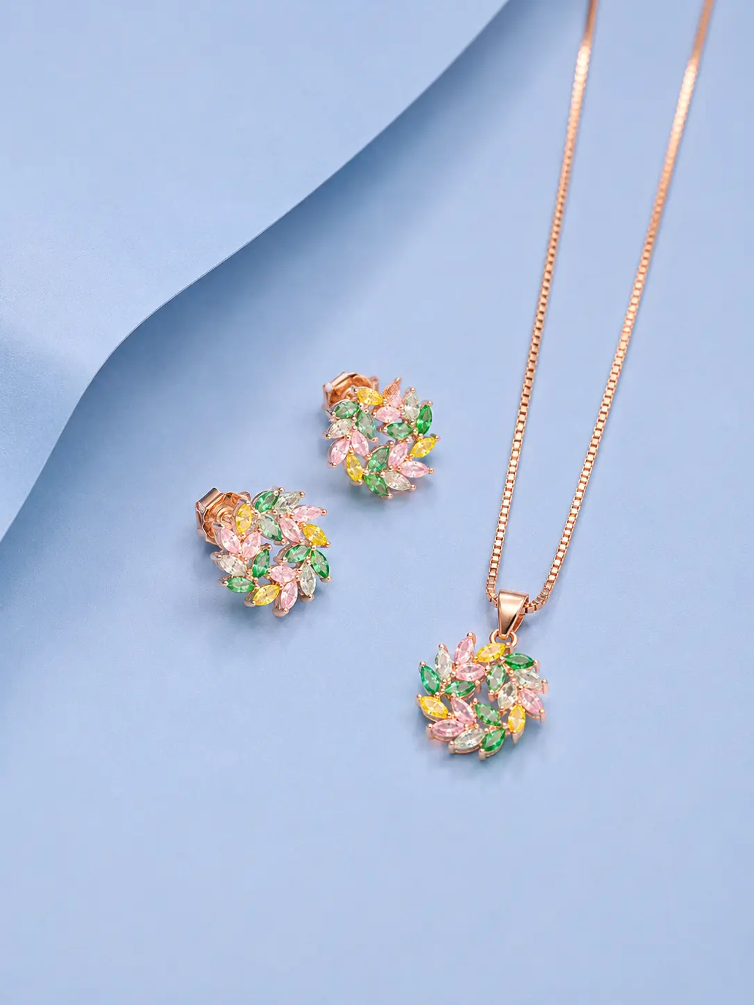 Round leef chain pendant earring rosegold Rose gold floral pendant and earrings set featuring multicolour zircon stones displayed on a soft pastel blue background.