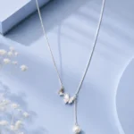 Silver butterfly pendant necklace with zircon accents and pearl drop displayed on a soft pastel blue luxury jewellery background.