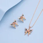 Rose gold butterfly pendant necklace with matching butterfly earrings featuring multicolour zircon stones displayed on a pastel blue background.