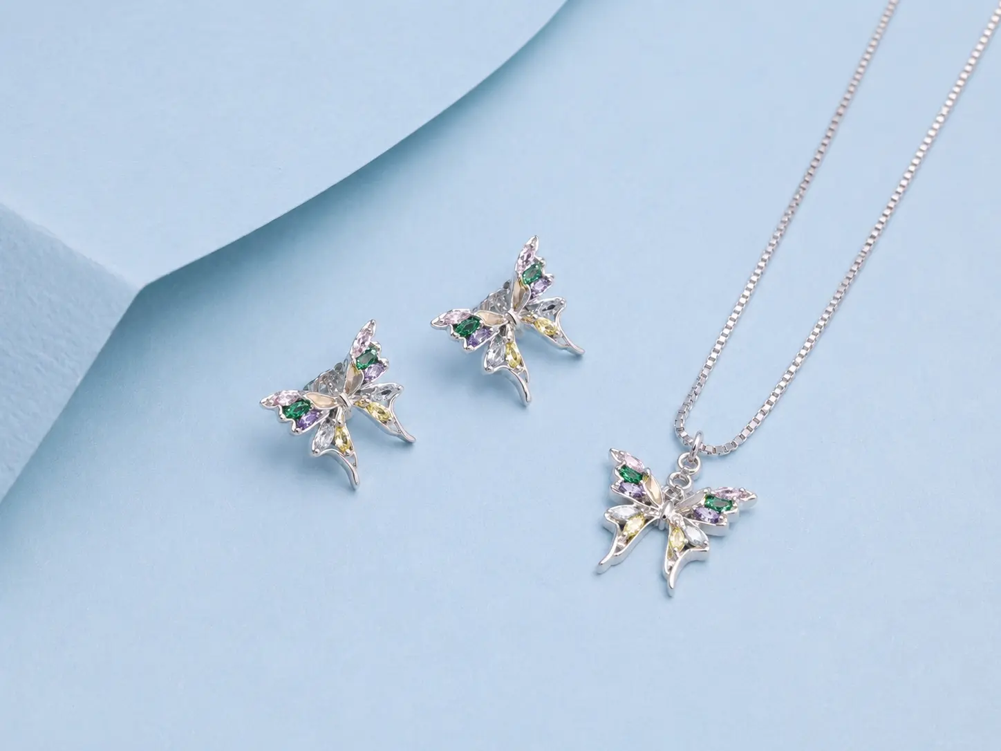 butterfly pendant earring silver Sterling silver butterfly pendant necklace with matching butterfly earrings featuring multicolour zircon stones on a pastel blue background.