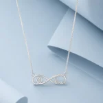 Sterling silver infinity necklace with zircon stone detailing and elegant “love” script pendant displayed on a soft pastel blue luxury background.