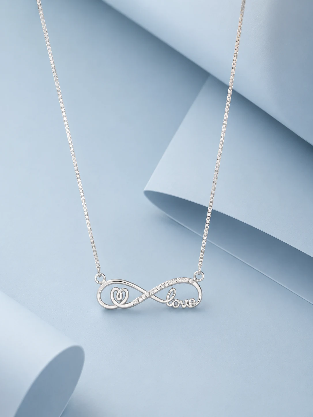heart love infinity silver Sterling silver infinity necklace with zircon stone detailing and elegant “love” script pendant displayed on a soft pastel blue luxury background.