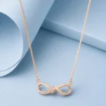 Rose gold infinity necklace with intertwined zircon-studded design displayed on a pastel blue background.