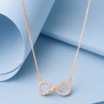 Rose gold twisted infinity necklace with zircon detailing displayed on a pastel blue geometric background.