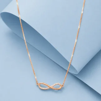 Rose gold infinity necklace with zircon stone detailing displayed on a pastel blue luxury background.