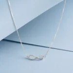 Sterling silver infinity necklace with zircon stone detailing displayed on a soft pastel blue background.