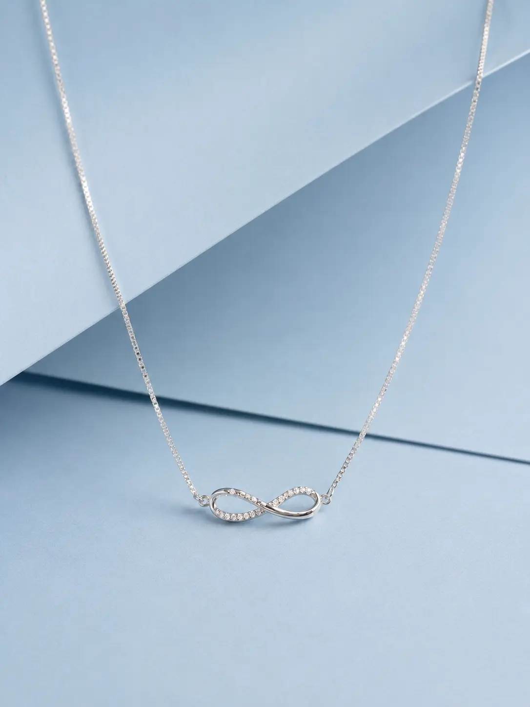 infinity stone silver Sterling silver infinity necklace with zircon stone detailing displayed on a soft pastel blue background.