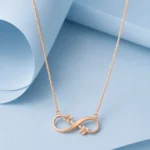 Rose gold infinity necklace with delicate leaf accents and zircon detailing displayed on a pastel blue background.