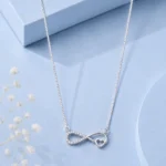 Silver infinity heart pendant necklace with zircon detailing displayed on a soft pastel blue luxury background.