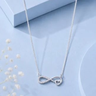 Silver infinity heart pendant necklace with zircon detailing displayed on a soft pastel blue luxury background.