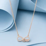 Rose gold plated sterling silver infinity necklace with zircon stone detailing, heart motif, and “Love” script displayed on a soft pastel blue luxury background.