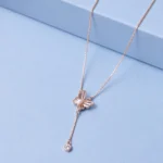 Rose gold butterfly pendant necklace with pearl detailing and zircon drop charm displayed on a soft pastel blue luxury background.