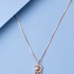 Rose gold dreamcatcher pendant necklace with pearl centerpiece and feather charms displayed on a pastel blue background.