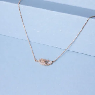 Rose gold feather-inspired necklace with zircon detailing and pearl accent displayed on a soft pastel blue background.