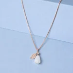 Rose gold floral pendant necklace with ivory flower charm and zircon detailing displayed on a soft pastel blue background.