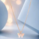 Rose gold butterfly pendant necklace with iridescent crystal wings displayed on a soft pastel blue luxury jewellery background.