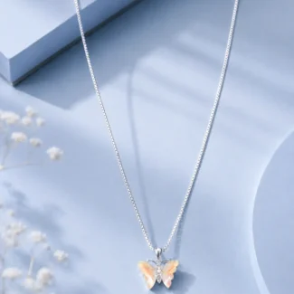Silver butterfly pendant necklace with iridescent crystal wings displayed on a soft pastel blue luxury jewellery background.