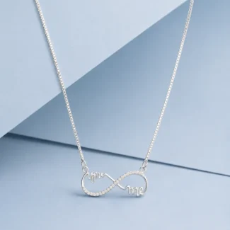 Sterling silver infinity necklace with “You & Me” lettering and zircon detailing displayed on a pastel blue luxury background.